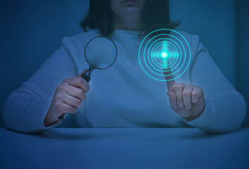 a woman sits at a table and holds a magnifying glass, with the other hand presses on a virtual...