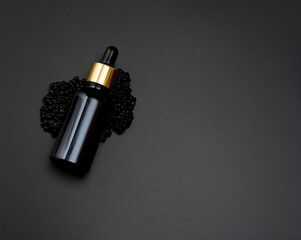 glass bottle with a pipette lies on a heap of black caviar, black background. Natural cometic....