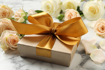 Golden gift box and beautiful roses on white marble table