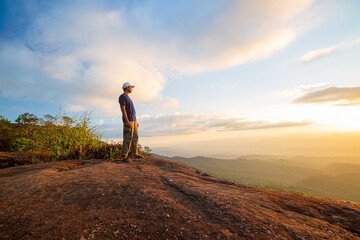 Fototapeta premium Young man with backpack standing with raised hands on top of a mountain and enjoying valley view