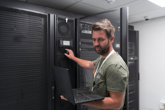 Data Center Engineer Using Laptop Computer Server Room Specialist Facility with Male System Administrator Working with Data Protection Network for Cyber Security or Cryptocurrency Mining Farm. 