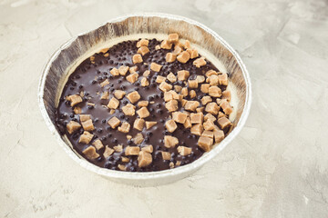 Cheesecake with chocolate frosting and salted caramel pieces on light gray background. Homemade dessert for birthday, festive party, engagement or Valentine day, selective focus, copy space
