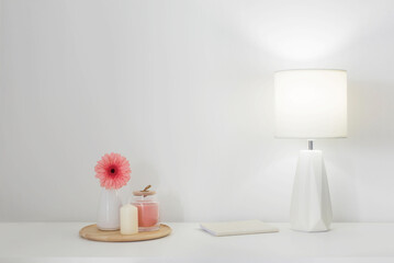 pink gerber in vase, candles and modern lamp on white shelf