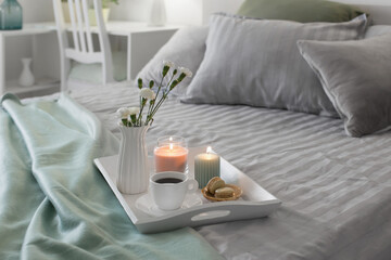 cup of coffee on wooden tray on bed with flowers and candles