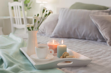 cup of coffee on wooden tray on bed with flowers and candles