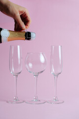 bottle of champagne in hand pouring into glasses, on a pink background. opening champagne in anticipation of the holiday