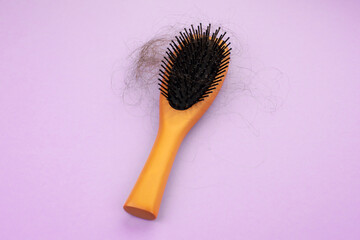 hair loss. wooden comb with burnt hair from stress or coronavirus on a purple background.