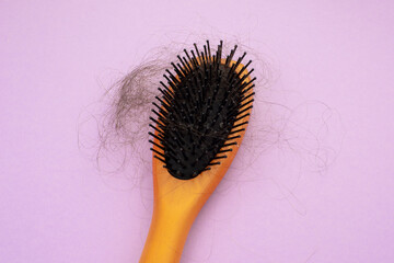 hair loss. wooden comb with burnt hair from stress or coronavirus on a purple background.