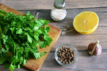 parsley on cutting board with pink salt, garlic, lemon and allspice on wooden background