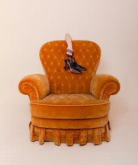 Tired woman holding shoes behind the sofa..While standing behind the yellow sofa. Photo in studio....