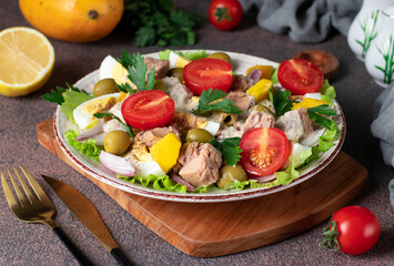 Salad with mango, tuna and cherry tomatoes served with green lettuce leaves in a plate on a brown background, Close-up