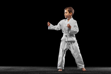 One little kid, boy, taekwondo athlete posing isolated over dark background. Concept of sport,...