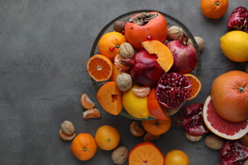 Many different seasonal fruits and walnuts in a plate on a beige table. Background with nuts, tangerines, pomegranates, grapefruits, persimmons and lemons