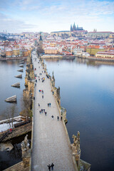 Naklejka premium People are walking on Charles bridge, whose rooftops are covered by snow, Prague in the winter