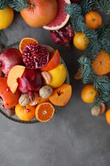 Naklejka na ściany i meble Many different seasonal fruits and walnuts in a plate on a beige table. Background with nuts, tangerines, pomegranates, grapefruits, persimmons and lemons