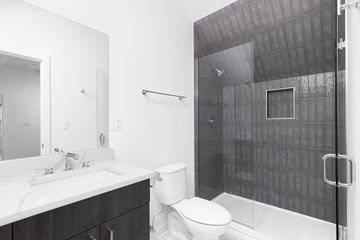 A renovated bathroom with a wood cabinet, chrome faucet, and a grey tiled shower.