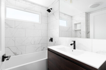 A renovated bathroom with a wood vanity cabinet, white marble sink and large marble tiles lining...