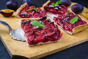 Traditioneller deutscher Zwetschgenkuchen mit aufgeschnittenen Pflaumen serviert als close-up auf einem rustikalen Holzbrett