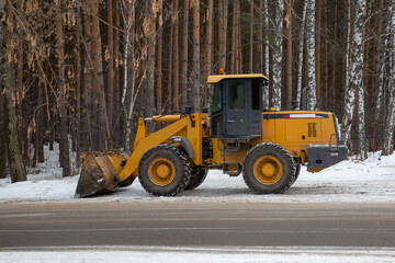 Tractor with mounted implements removes snow in winter in the city