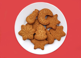 Gingerbread cookies, different gingerbread shapes on a plate, on a red background