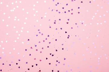 Purple glittering hearts on a pink pastel background. Festive background.