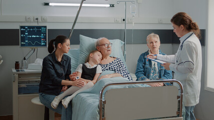 Little girl and mother visiting grandpa in hospital ward while doctor consults him for recovery. Medic explaining diagnosis to ill patient and family in visit at clinic. Physician at checkup