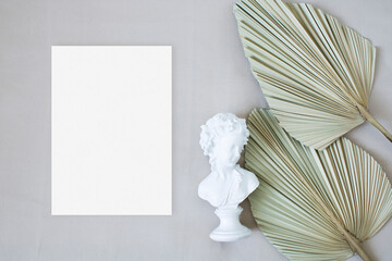 Top view mockup wedding card with leaf palm and statuette on the beige background