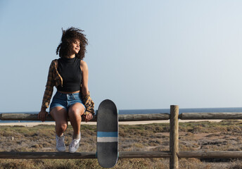 Young skater woman with afro hair sitting on a fence outdoors - Powered by Adobe