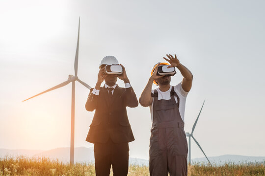 African american businessman and indian engineer wearing VR headset during meeting on farm with wind turbines. Innovative technologies and alternative energy concept.