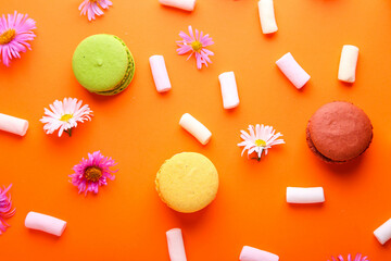 Obraz na płótnie Canvas Beautiful composition with macaroons, flowers and marshmallows on a orange background. Top view