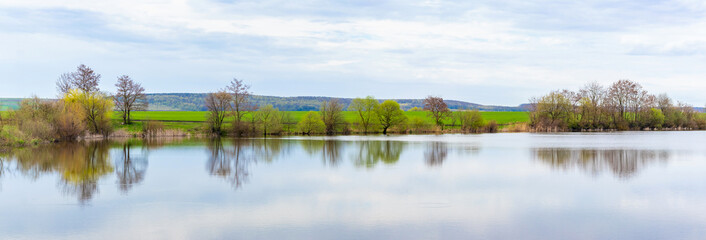 Spring landscape with river and trees reflected in water in light colors