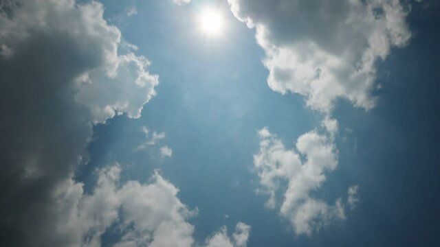 White light clouds quickly fly, cover bright sun in zenith sometimes, time lapse shot. Low angle camera look straight upwards to blue sky and fast moving and curling clouds