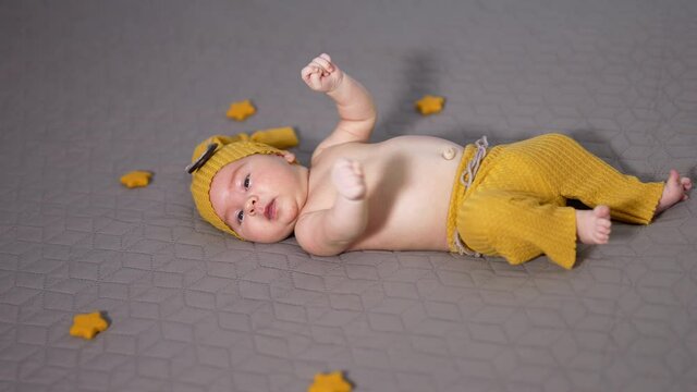 Cute tiny child moving his hands actively. Boy in yellow costume and surrounded by small toy stars on the grey blanket.