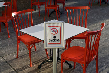 No smoking sign at cafe with empty red chairs.