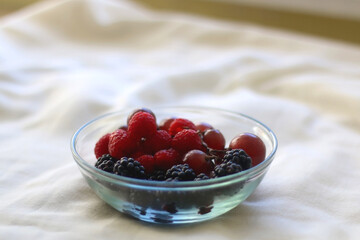 Small glass bowl filled with grapes, blackberries and raspberries.  Selective focus. 