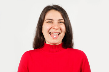 A healthy young woman in red with pills on her tongue smiles and looks into the camera on a white background