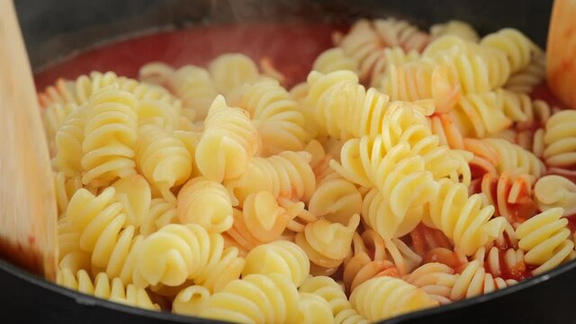 Stir pasta fusilli and tomato sauce in pan, close up. Cooking traditional italian dinner. 4K UHD video