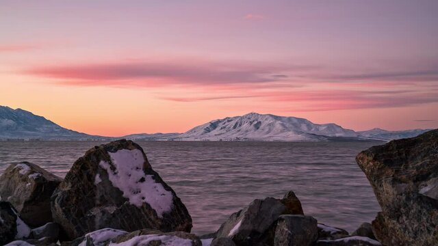 Sunrise timelapse looking past rocks on Utah Lake in winter with West Mountain in the distance.