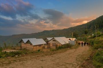 Fototapeta na wymiar Houses beside road leading to mountain, Silerygaon Village at sunset, Sikkim; Shot at golden hour.