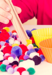 Little baby boy playing with small pompoms, wooden tongs and cups. Development of kids motor skills, coordination and logical thinking