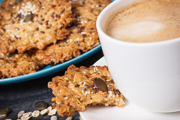 Cup of coffee with milk and fresh baked oatmeal cookies on blue plate. Delicious crunchy dessert