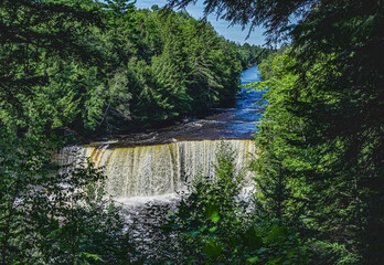 Long View of Higher Falls of Tahquamenon Falls; wide river rushing over cliff with forest on both sides in late summer. 195
