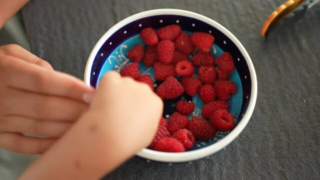 Child hands grabbing rasberries from bowl
