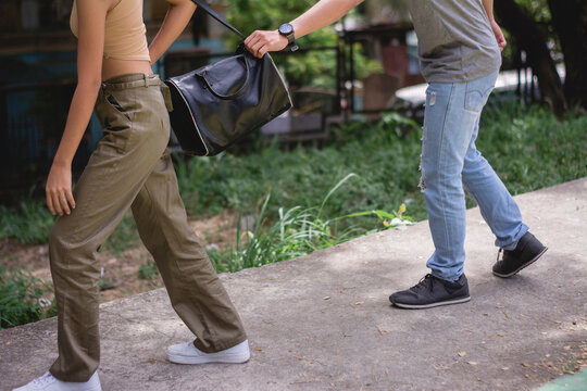 A thief attempts to quickly cut the strap of an woman's handbag. A sneaky theft in progress in broad daylight.