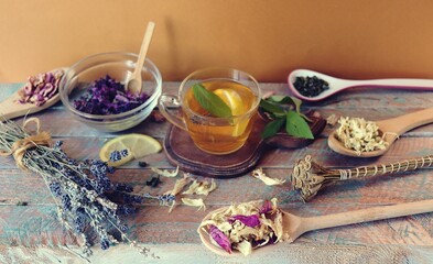 Cup of green tea with mint and lemon, dry petals of useful plants on a wooden table, banner