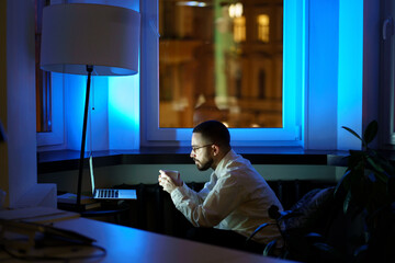 Young man drink coffee refreshing working in empty office overtime. Successful male entrepreneur...