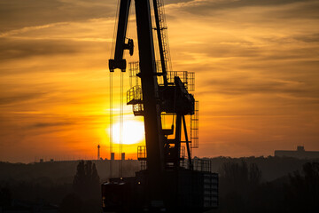 Kran an der Havel entlädt im Hafen ein Schiff im Sonnenaufgang.