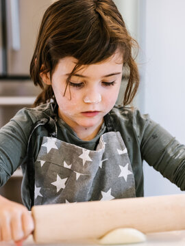 Cute girl kneading dough with rolling pin