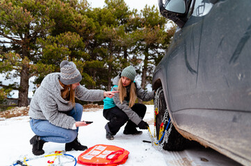 Women friends trying to put snow chain on wheel tire