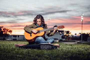 woman learns to play guitar in a park at dusk